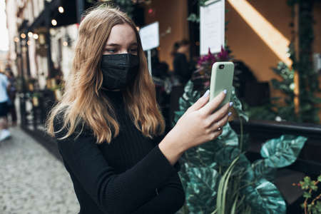 Young woman having video call talking while walking downtown wearing the face mask to avoid virus infection and to prevent the spread of disease in time of coronavirusの写真素材