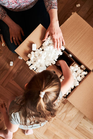 Woman unpacking a cardboard box parcel in room at home. Little girl waiting for opening a gift in...