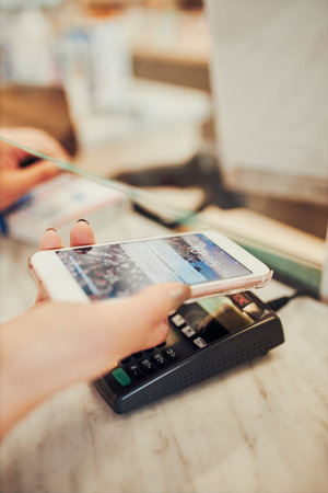 Woman paying for medicines at pharmacy using contactless method of payment via mobile phone. Woman...