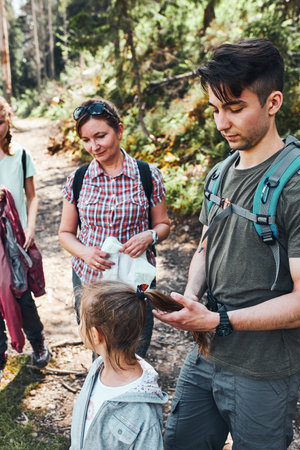Family with backpacks hiking in a mountains actively spending summer vacation together walking on forest path talking and admiring nature mountain landscapesの写真素材