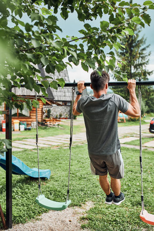 Young man doing pull-ups on pull-up horizontal bar during his calisthenics workout on a camping...