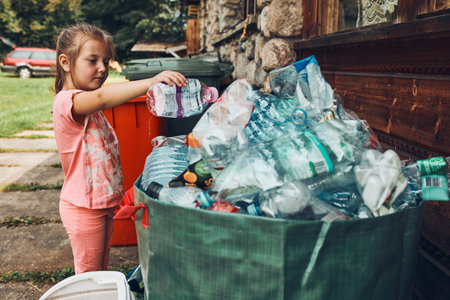 Child little girl throwing out plastic bottle to big container full of plastic wasteの写真素材
