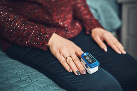 Woman measuring the degree of oxygen saturation of the blood and heart rate at home using pulse...