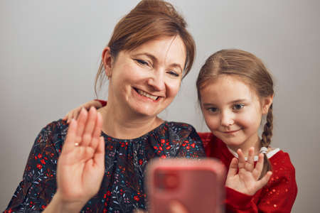 Mother with her little daughter making video call using mobile phone. Keeping distance. Woman and little girl talking with relatives. Cheerful family having fun taking selfie photo using smartphone. Connecting remotely with familyの写真素材