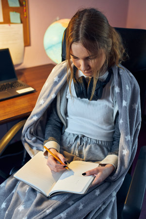 Student learning remotely from home. Young woman having classes online, making notes, reading and...