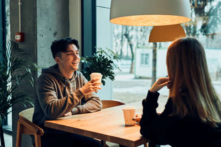 Friends having a chat, talking together, drinking coffee, sitting in a cafe. Young man and woman having a break, relaxing in cafeの写真素材