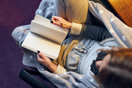 Student learning at home. Young woman making notes, reading and learning from notepad sitting in bed...