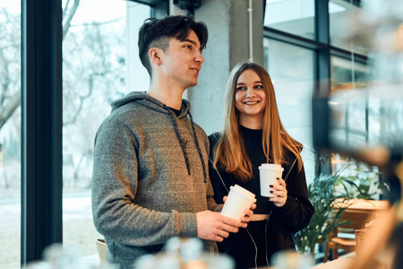 Friends doing shopping in a coffee shop. Young man and woman having chat while picking out the pastry, bakery's goods and hot drinks standing at counter in a coffee shop. People buying coffee and sweet snacks to goの写真素材