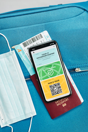 Digital covid certificate. Vaccination digital pass. Digital medical pass, passport, airplane ticket and face mask on travel bag. Digital covid vaccination pass on mobile as medical pass for travel during covid-19 pandemic. Preparing for travelの写真素材