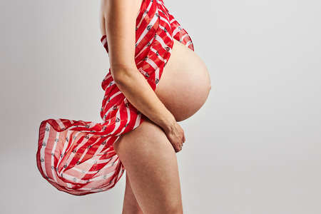 Pregnant woman touching her tummy standing over plain background. Pregnancy, expectation, motherhood conceptの写真素材