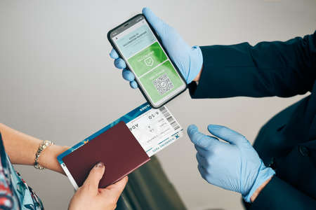 Digital covid certificate. Covid vaccination digital pass. Woman passenger holding digital medical pass on her mobile phone, passport and airplane ticket. Traveler showing digital covid test result as medical pass for travel during covid-19 pandemicの写真素材
