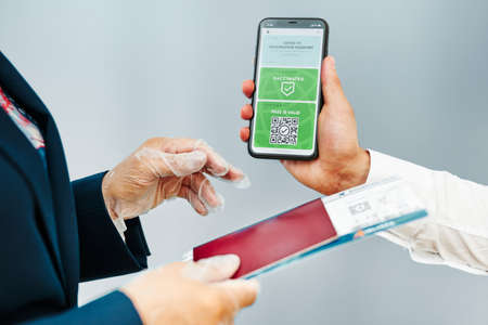 Digital covid certificate. Covid vaccination digital pass. Woman passenger holding digital medical pass on her mobile phone, passport and airplane ticket. Traveler showing digital covid test result as medical pass for travel during covid-19 pandemicの写真素材