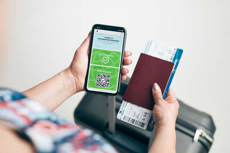 Digital covid certificate. Covid negative rapid digital test pass. Woman passenger holding digital medical pass on her mobile phone, passport and airplane ticket. Traveler showing digital covid test result as medical pass for travel during covid-19 pandemicの写真素材