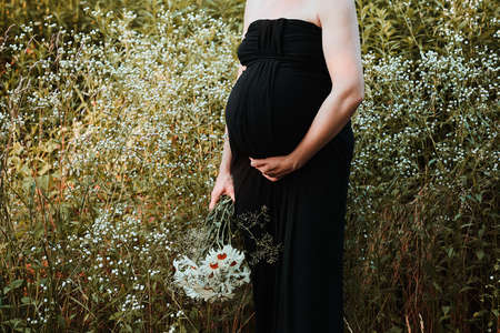 Pregnant woman hugging her tummy standing outdoors surrounded by nature. Pregnancy, expectation, motherhood conceptの写真素材