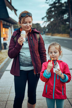 Mother and her daughter enjoying ice cream walking through town afternoonの写真素材