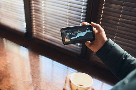 Person investing trading on stock cryptocurrency market using investing application on smartphone. Stock market investment in hand. Trader holding mobile phone looking at candle chartの写真素材