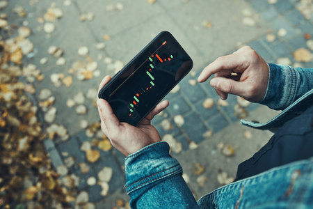 Person investing trading on stock cryptocurrency market using investing application on smartphone. Stock market investment in hand. Trader holding mobile phone looking at candle chartの写真素材