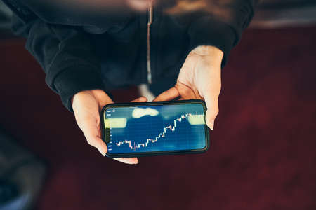 Person investing trading on stock cryptocurrency market using investing application on smartphone. Stock market investment in hand. Trader holding mobile phone looking at candle chartの写真素材