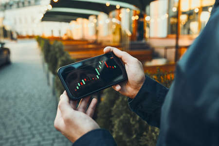 Person investing trading on stock cryptocurrency market using investing application on smartphone. Stock market investment in hand. Trader holding mobile phone looking at candle chartの写真素材
