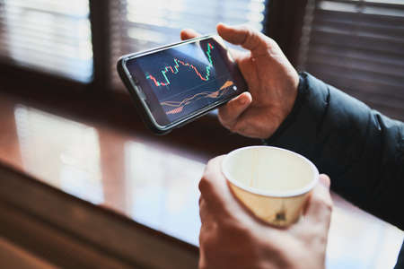 Person investing trading on stock cryptocurrency market using investing application on smartphone. Stock market investment in hand. Trader holding mobile phone looking at candle chartの写真素材