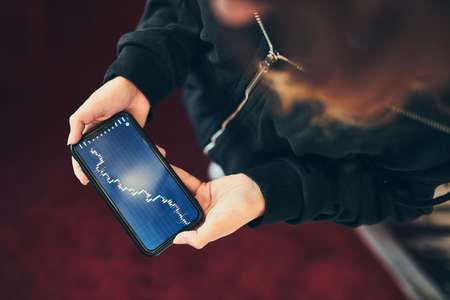 Person investing trading on stock cryptocurrency market using investing application on smartphone. Stock market investment in hand. Trader holding mobile phone looking at candle chartの写真素材