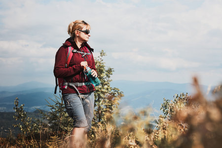 Woman with backpack hiking in mountains, spending summer vacation close to nature. Woman walking on...