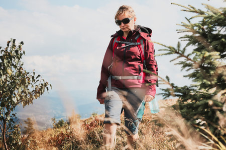 Woman with backpack hiking in mountains, spending summer vacation close to nature. Woman walking on...
