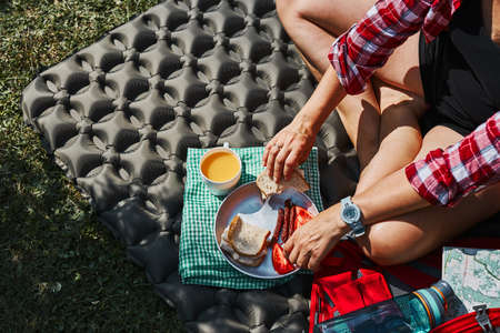 Woman having breakfast sitting by tent at camping. Female actively spending summer vacations close to nature outdoors. Concept of camp lifeの写真素材