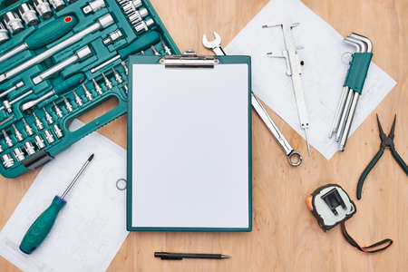 Workshop table with many tools. Wrench, spanner, calliper and ratchet with many attachments. Clipboard with white paper. Work tools. Universal tool set. Professional equipment. Background. Copy spaceの写真素材