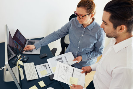 Businesswoman discussing financial data with her colleague standing at desk in office. Woman...