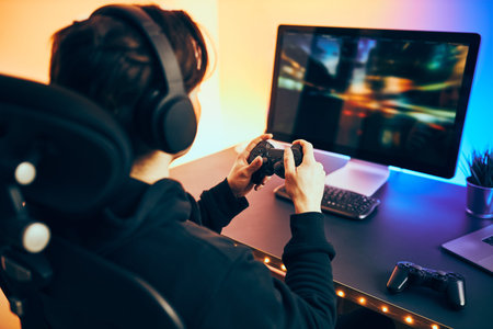 Man playing video game at home. Gamer holding gamepads sitting at front of screen. Streamer playing...