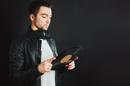 Handsome man looking at vinyl record. Rock style. Vintage music style. Male wearing black jacket...
