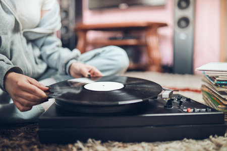 Young woman listening to music from vinyl record player. Retro and vintage music style. Girl holding analog record album sitting in room at home. Female enjoying music from old record collectionの写真素材