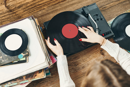 Young woman listening to music from vinyl record player. Playing music on turntable player. Female enjoying music from old record collection at home. Stack of analog vinyl records. Retro and vintage music style. Music Passion and hobbyの写真素材