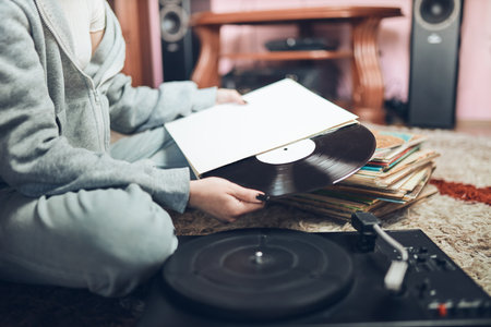 Young woman listening to music from vinyl record player. Retro and vintage music style. Girl holding analog record album sitting in room at home. Female enjoying music from old record collectionの写真素材