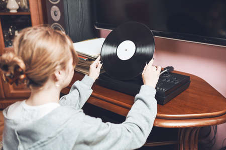 Young woman listening to music from vinyl record player. Retro and vintage music style. Girl holding analog record album sitting in room at home. Female enjoying music from old record collectionの写真素材