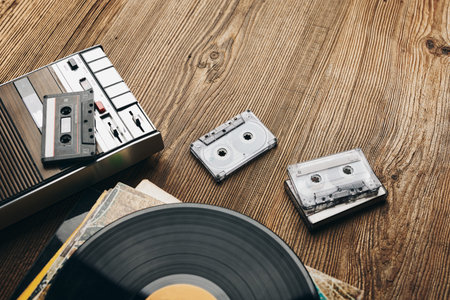Vinyl records, cassette tapes and cassette recorder on wooden table. Retro music style. 80s music...