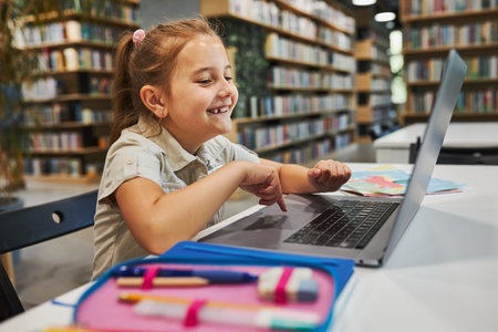 Cheerful student doing her homework using laptop in after school club at primary school. Back to...
