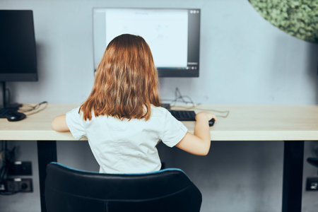 Child learning to use technology in classroom at primary school. Schoolgirl using computer on...