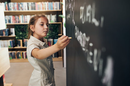 Little girl writing on blackboard. Smart student put solve on chalkboard. Back to school. Child...