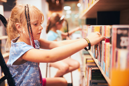 Schoolgirls looking for books in school library. Students choosing books. Elementary education. Doing homework. Learning from books. Back to schoolの写真素材