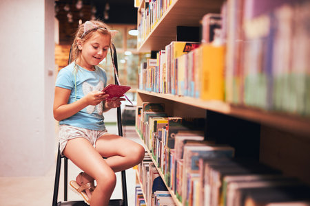 Schoolgirl looking for book in school library. Student choosing book for reading. Books on shelves in bookstore. Learning from books. Back to school. Elementary education. Doing homeworkの写真素材