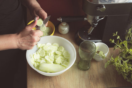 Cooking at home. Close up of female hand cutting cucumber to a bowl. Making salad from fresh cucumbers from home garden. Healthy diet. Preparing mealの写真素材