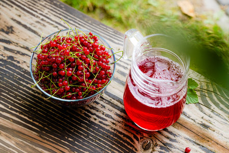 Fresh red currant in bowl and red currant beverage on wooden table. Fruits from home garden. Summer refreshments. Soft drink. Red currant compote. Healthy food. Homemade healthy drink. Seasonal fruitsの写真素材