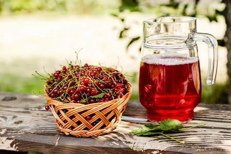 Fresh red currant in basket and red currant beverage on wooden table. Fruits from home garden. Summer refreshments. Soft drink. Red currant compote. Healthy food. Homemade healthy drink. Seasonal fruitsの写真素材