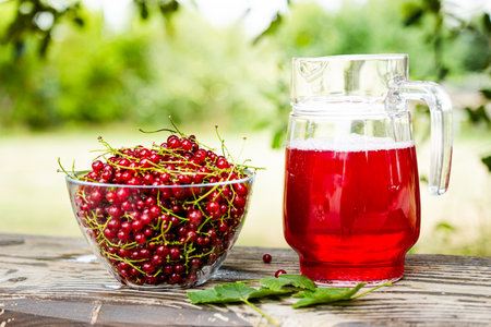 Fresh red currant in bowl and red currant beverage on wooden table. Fruits from home garden. Summer refreshments. Soft drink. Red currant compote. Healthy food. Homemade healthy drink. Seasonal fruitsの写真素材