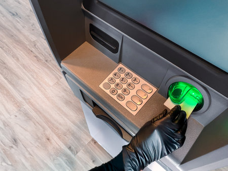Thief hand with black glove stealing money. Burglar committing robbery. Financial crime. Hacking ATM machine. Breaking system. Withdrawing cash at ATM from bank account using stolen debit card. Stealing cash from bank account. Illegal financial transaction conceptの写真素材