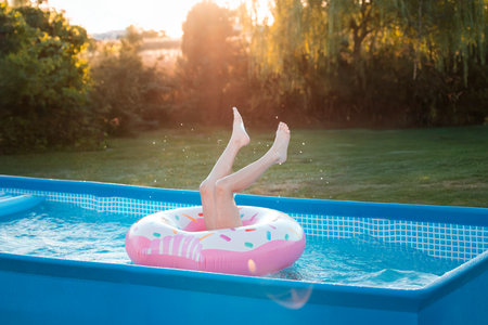 Child doing hand stand in home pool. Playing in swimming pool in backyard. Summer water fun. Joyful child enjoys splashing in a pool. Child playing in pool at home. Splashing in pool in garden backyard. Playing with inflatable toys. Summer sunny day outdoors on home yard. Swimming pool at homeの写真素材