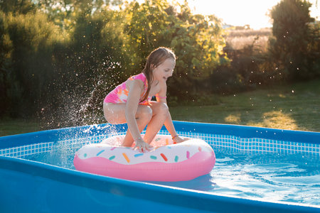 Playing in swimming pool in backyard. Summer water fun. Joyful child enjoys splashing in a pool. Child playing in pool at home. Splashing in pool in garden backyard. Playing with inflatable toys. Summer sunny day outdoors on home yard. Swimming pool at homeの写真素材