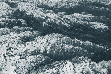 Aerial view of high rocky mountains covered with snow. Alpine landscape. Beauty in nature. Inaccessible mountain peaks. Harsh climate. Looking at the Earth from an airplane window. Aerial view of the landの写真素材